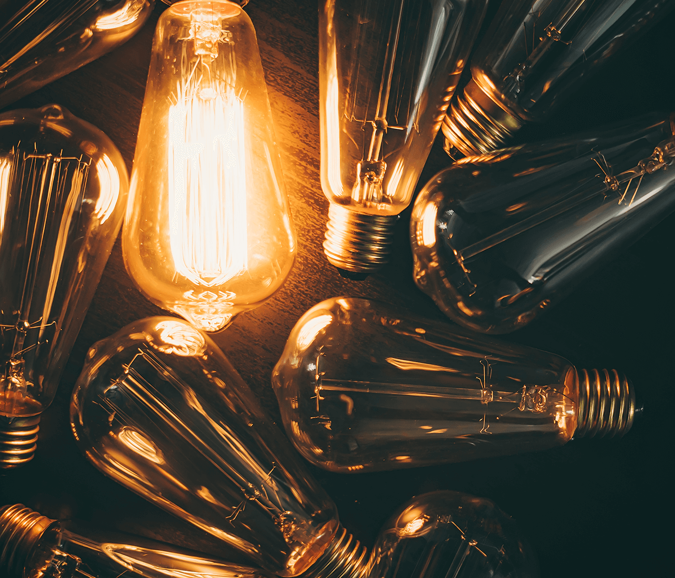 pile of long light bulbs on dark background, one is on